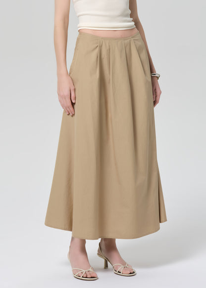 Woman wearing a beige top and long skirt on a grey background