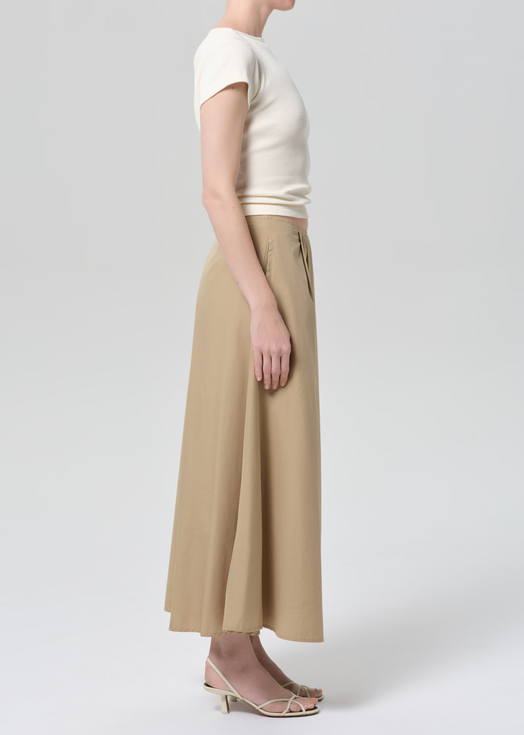 Woman wearing a beige top and long skirt on a grey background