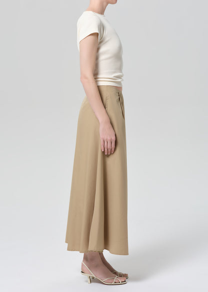 Woman wearing a beige top and long skirt on a grey background