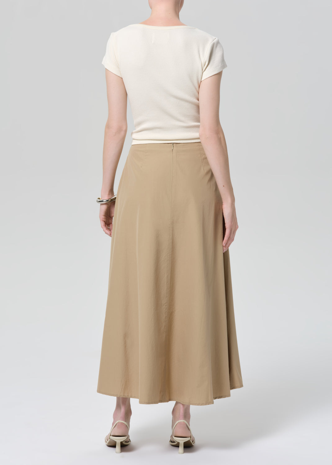 Woman wearing a beige top and long skirt on a grey background
