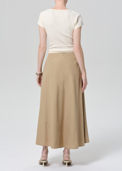 Woman wearing a beige top and long skirt on a grey background