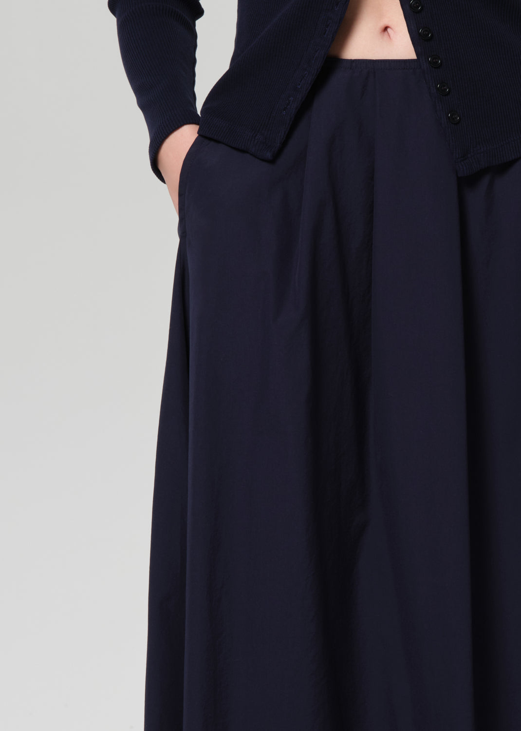 Person wearing a navy cardigan and long skirt on a grey background