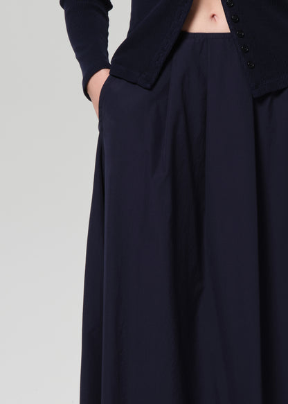 Person wearing a navy cardigan and long skirt on a grey background