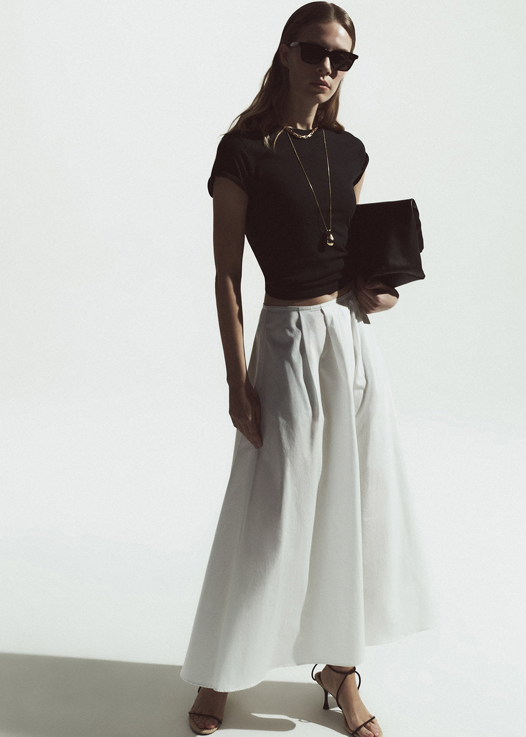 Woman wearing a black top and white pants against a white background