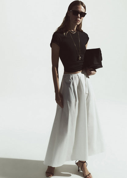Woman wearing a black top and white pants against a white background