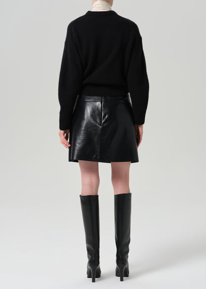 A model shown from the back wearing a black knit sweater, a black faux-leather mini skirt, and black knee-high heeled boots against a grey background.