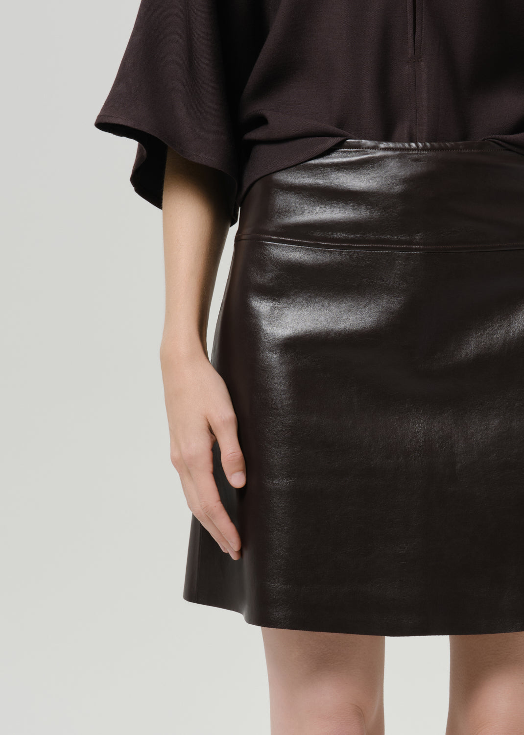 Person wearing a dark brown leather mini skirt on a grey background