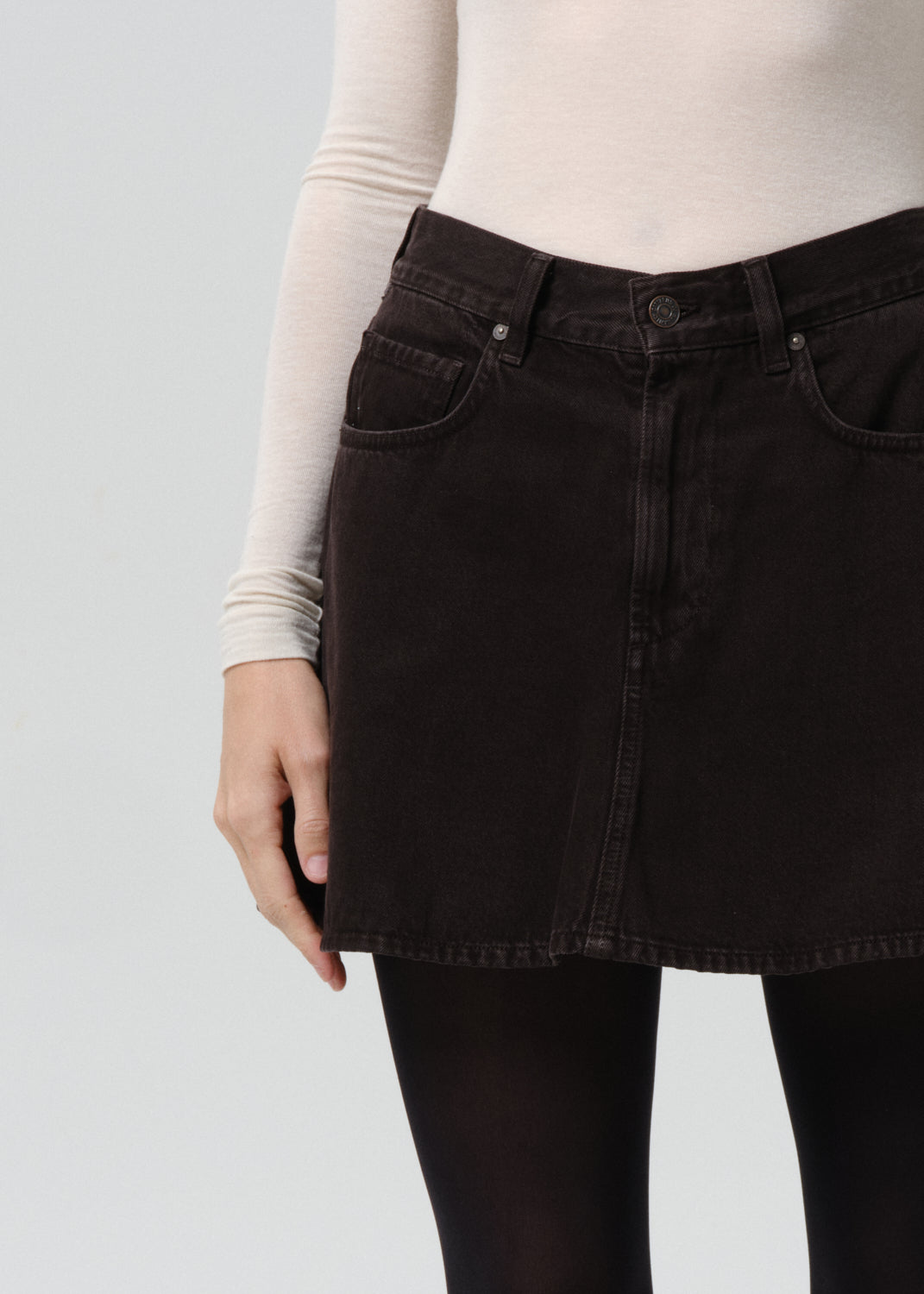Person wearing a black denim skirt with a grey background