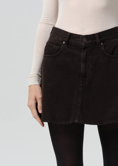 Person wearing a black denim skirt with a grey background