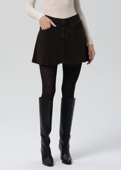 Person wearing a black skirt, black tights, and black knee-high boots on a grey background