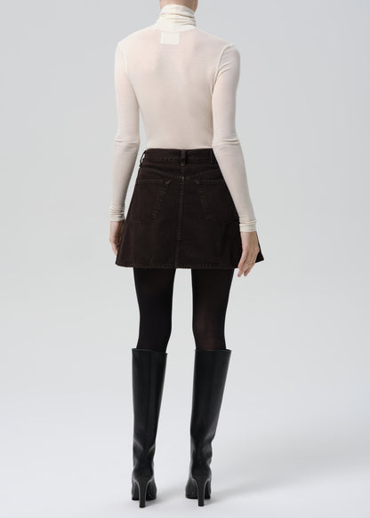 Person wearing a beige turtleneck, black skirt, and black knee-high boots on a grey background