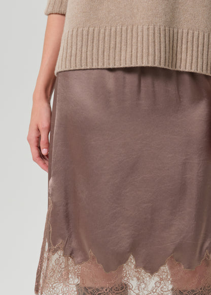 Close-up of a taupe brown satin midi skirt with a scalloped lace hem, styled with a beige ribbed knit sweater.