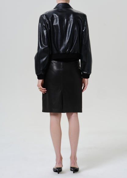 Woman wearing a black leather pencil skirt with a black leather jacket viewed from the back on a grey background.