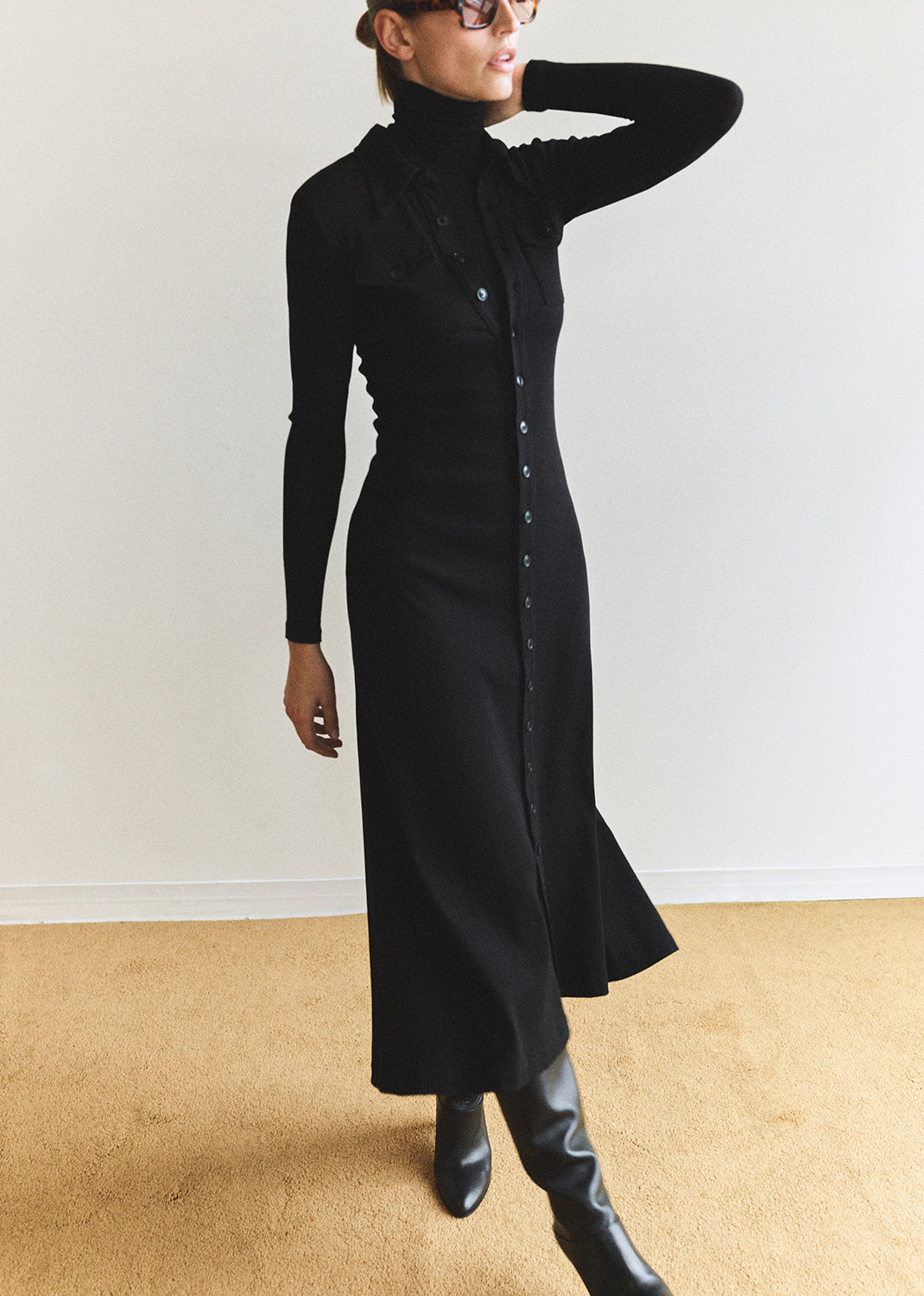 Person wearing a long black dress with a high collar against a plain background