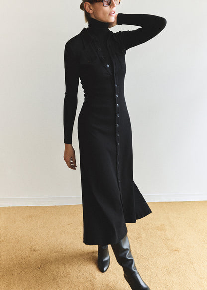 Person wearing a long black dress with a high collar against a plain background