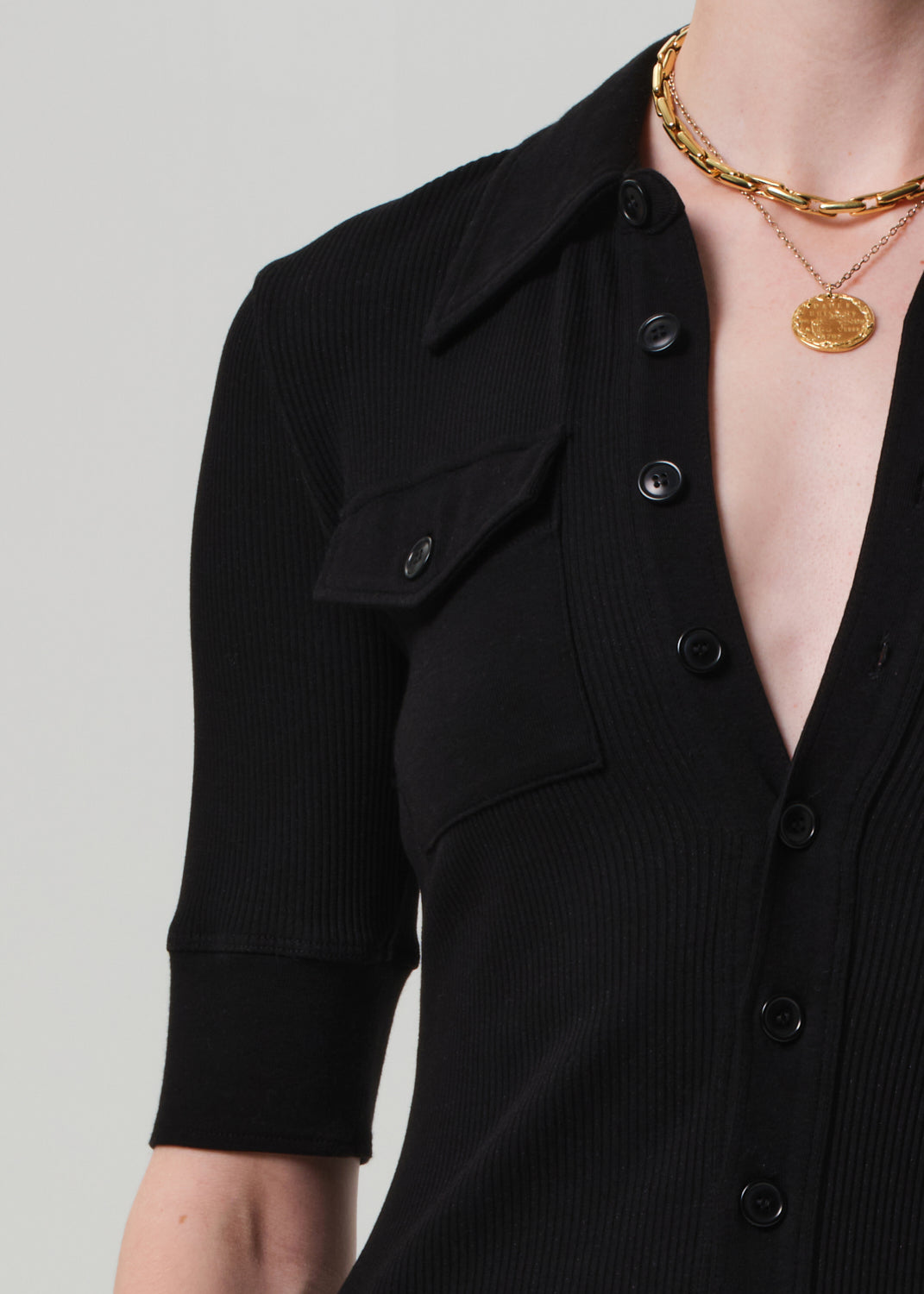 Black button-up shirt with a plunging neckline and gold jewelry on a neutral background