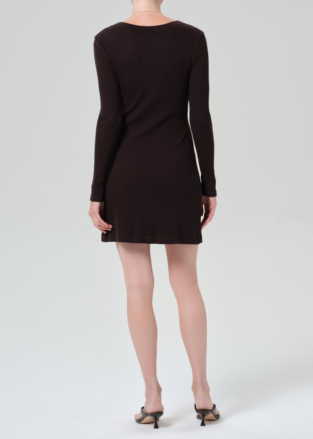 Person wearing a brown long-sleeve dress on a grey background
