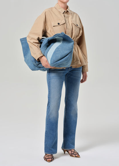Person wearing a beige jacket and blue jeans holding a denim bag 