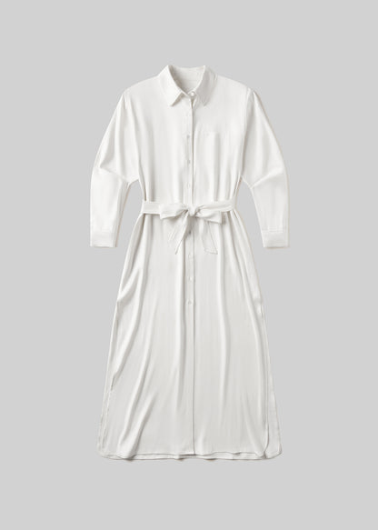 White long sleeve midi shirt dress with a pointed collar, front button closure, single chest pocket, and self-tie waist belt, front flat lay view on a grey background.