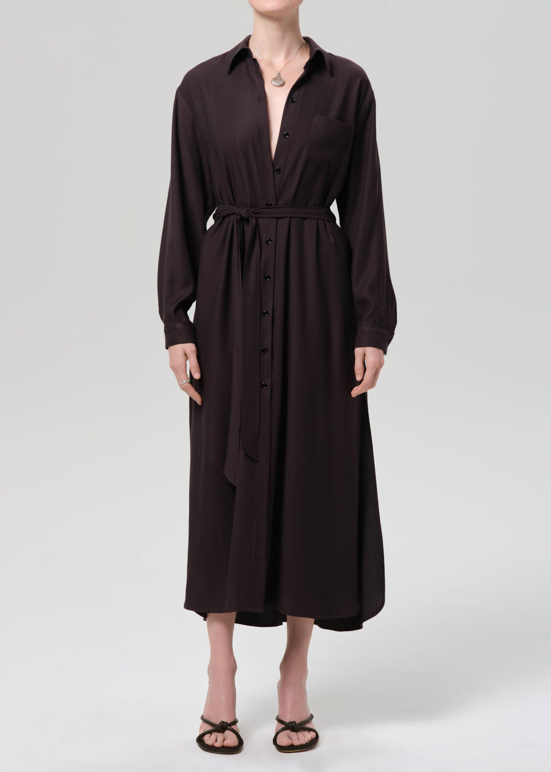 Person wearing a black dress with a belt on a grey background