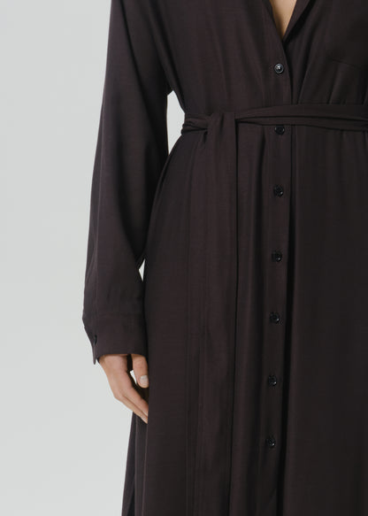 A close-up of a dark brown long-sleeve button-front dress with a matching waist tie, shown on a model against a grey background.