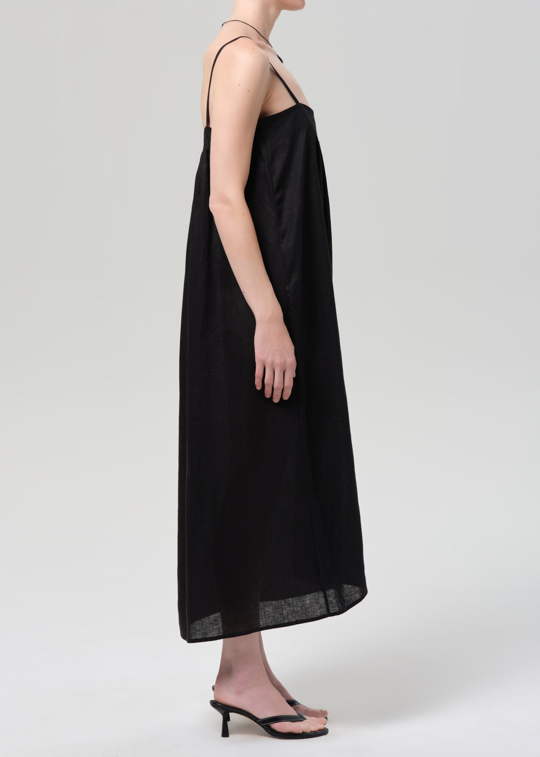 Person wearing a black linen dress on a grey background
