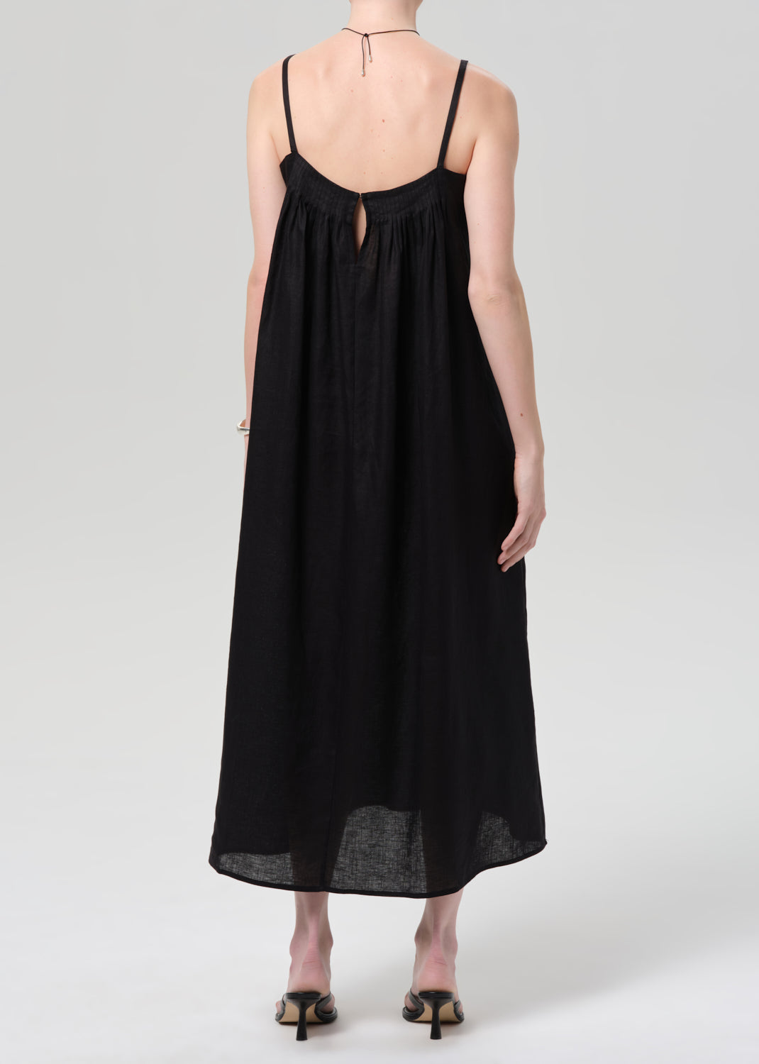 Person wearing a black linen dress on a grey background