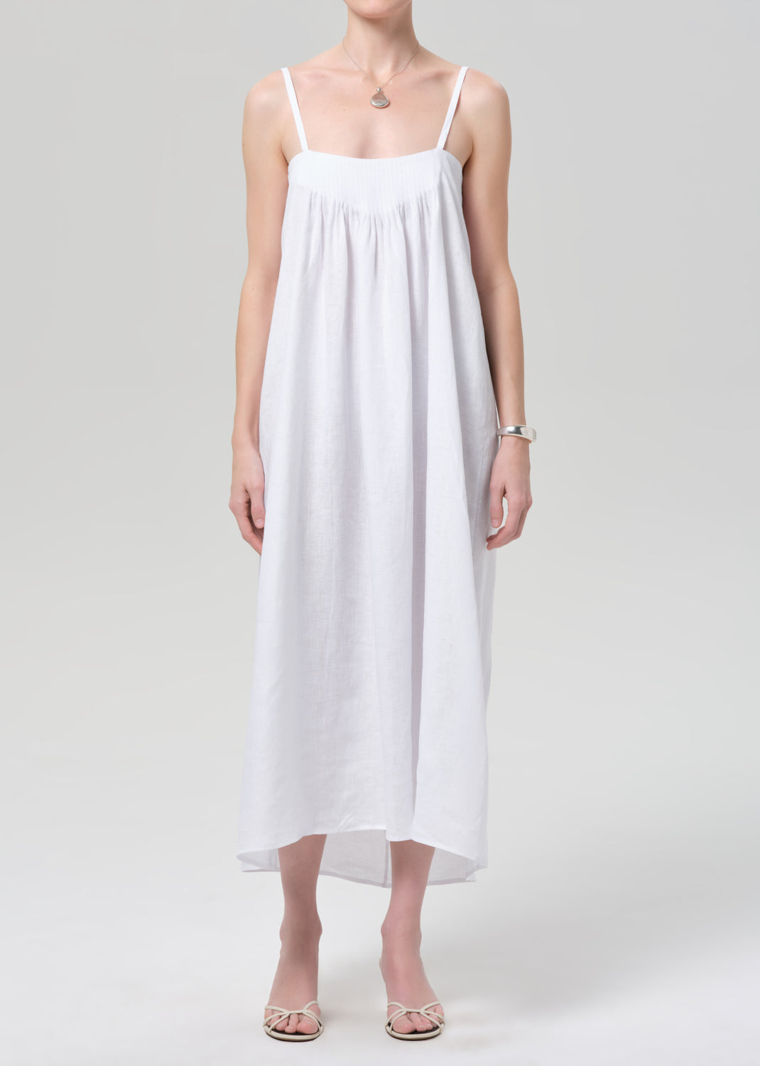 Woman wearing a white slip linen dress on a plain background