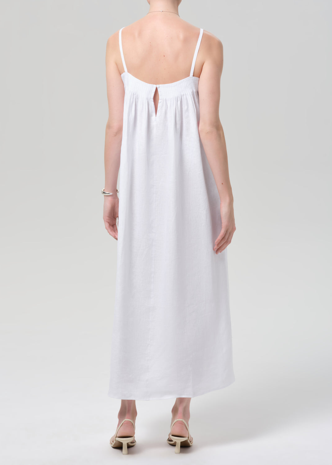 Woman wearing a white slip linen dress on a plain background