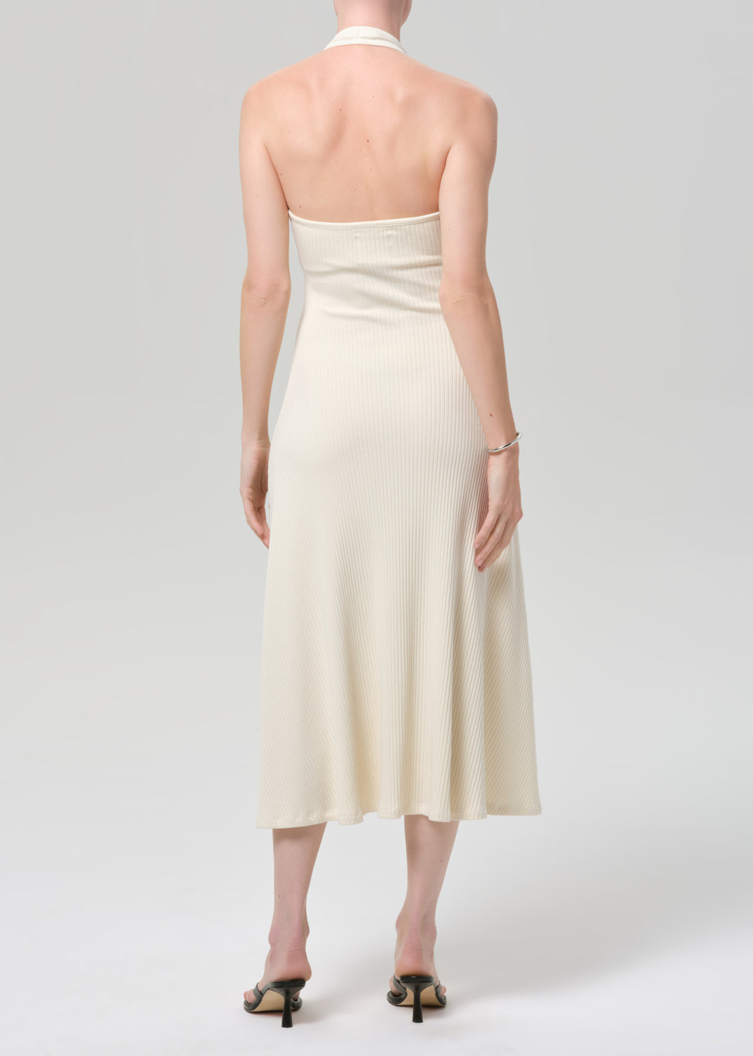 Woman wearing a cream halter neck dress on a plain background