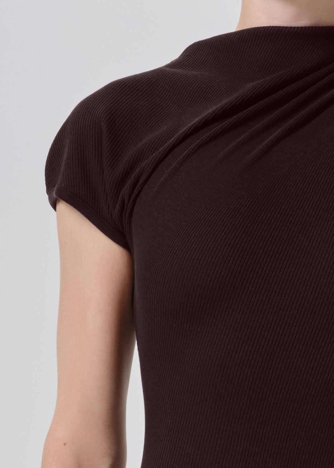 Close-up of a person wearing a dark brown ribbed short-sleeve top, showing the back and shoulder area against a grey background.
