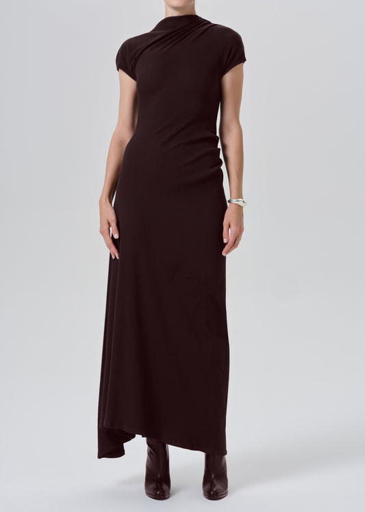 A model wearing a dark brown, short-sleeved mock-neck maxi dress with a draped, gathered bodice, paired with dark brown pointed-toe boots against a grey background.