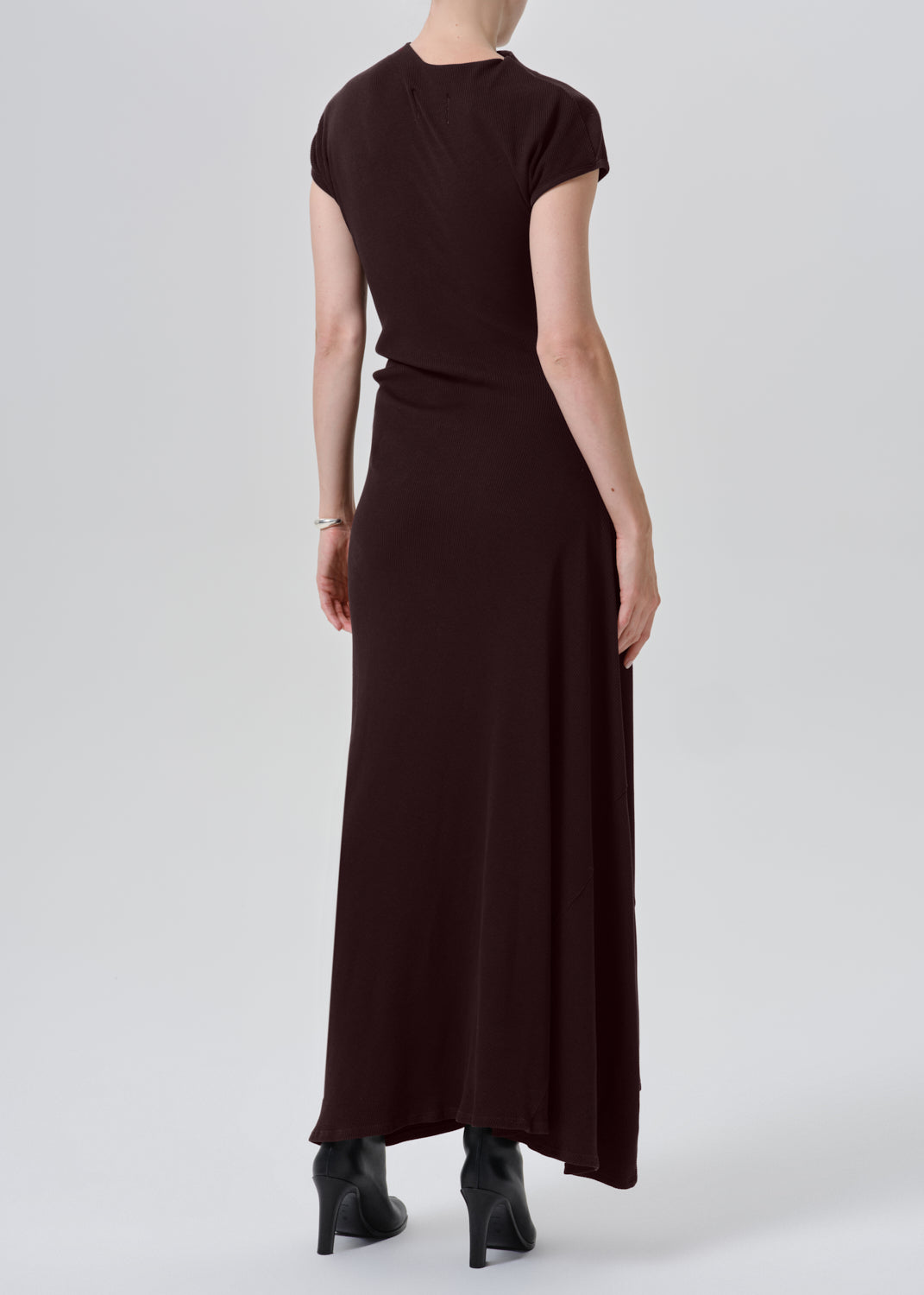 A woman shown from the back wearing a dark brown short-sleeve maxi dress and black pointed-toe heels against a grey background.
