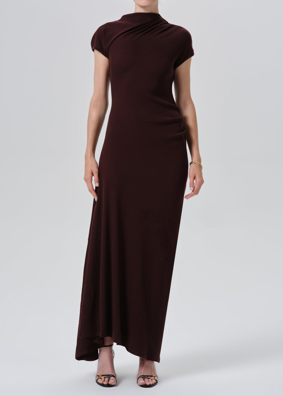 A woman modeling a dark brown, knee-length dress with a draped mock neck and short cap sleeves, shown from the back against a grey background.