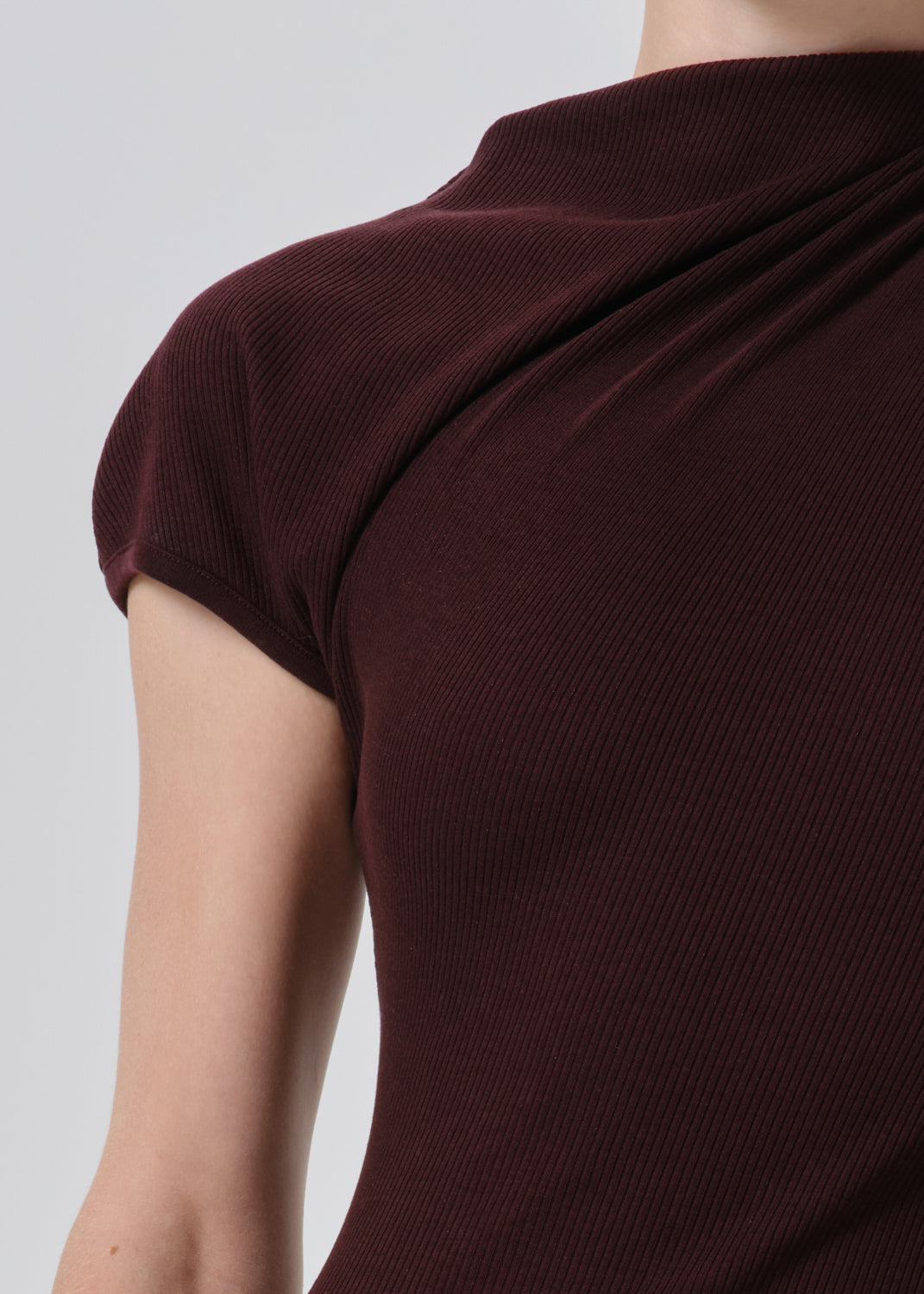 Close-up of a person wearing a ribbed knit top in deep burgundy, showing the shoulder, sleeve, and upper torso against a grey background.