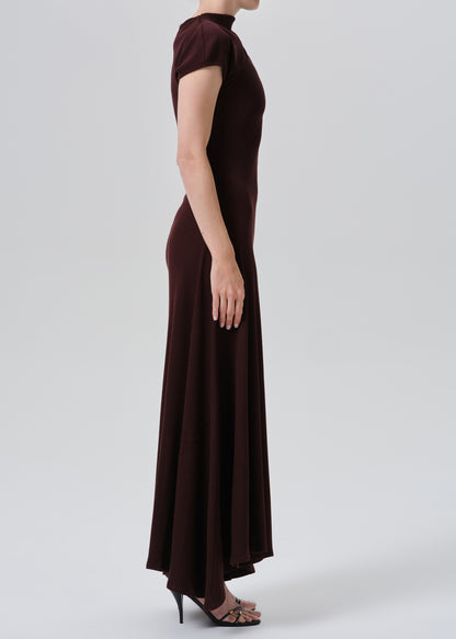A woman modeling a dark burgundy maxi dress with short sleeves, a mock neck, and a fitted silhouette, shown in profile against a grey background.