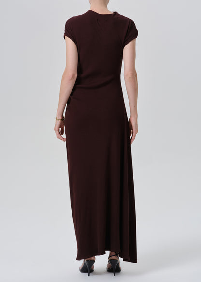 A woman viewed from the back wearing a dark brown short-sleeve maxi dress and black heels, standing against a grey background.