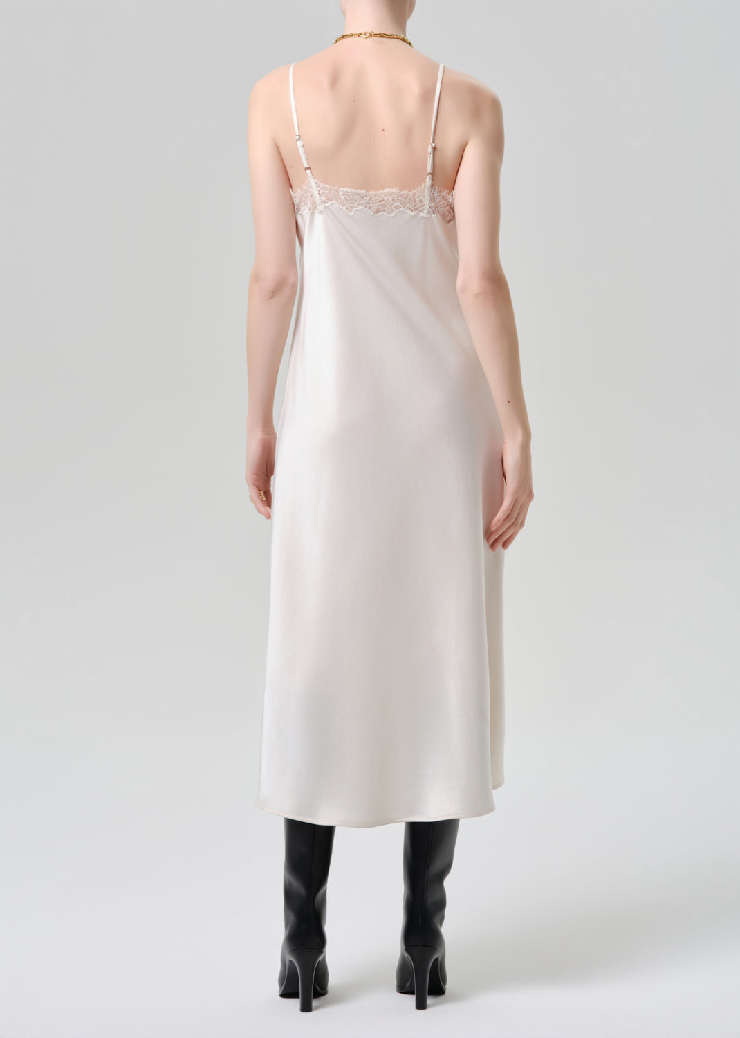 Woman wearing a white slip dress with thin straps on a grey background