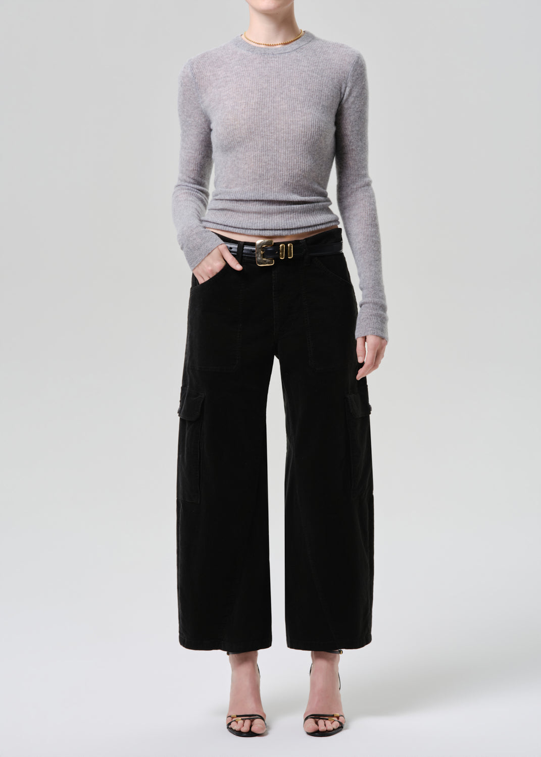Person wearing a grey sweater and black cargo pants on a grey background