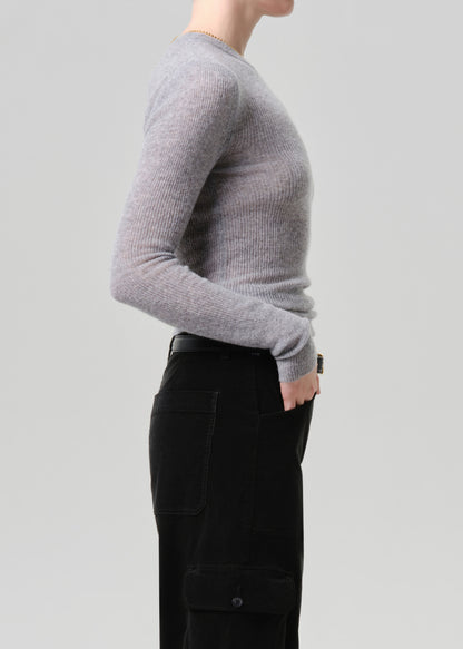 A side-profile view of a person wearing a light grey ribbed knit long-sleeve sweater and black cargo pants against a grey background.