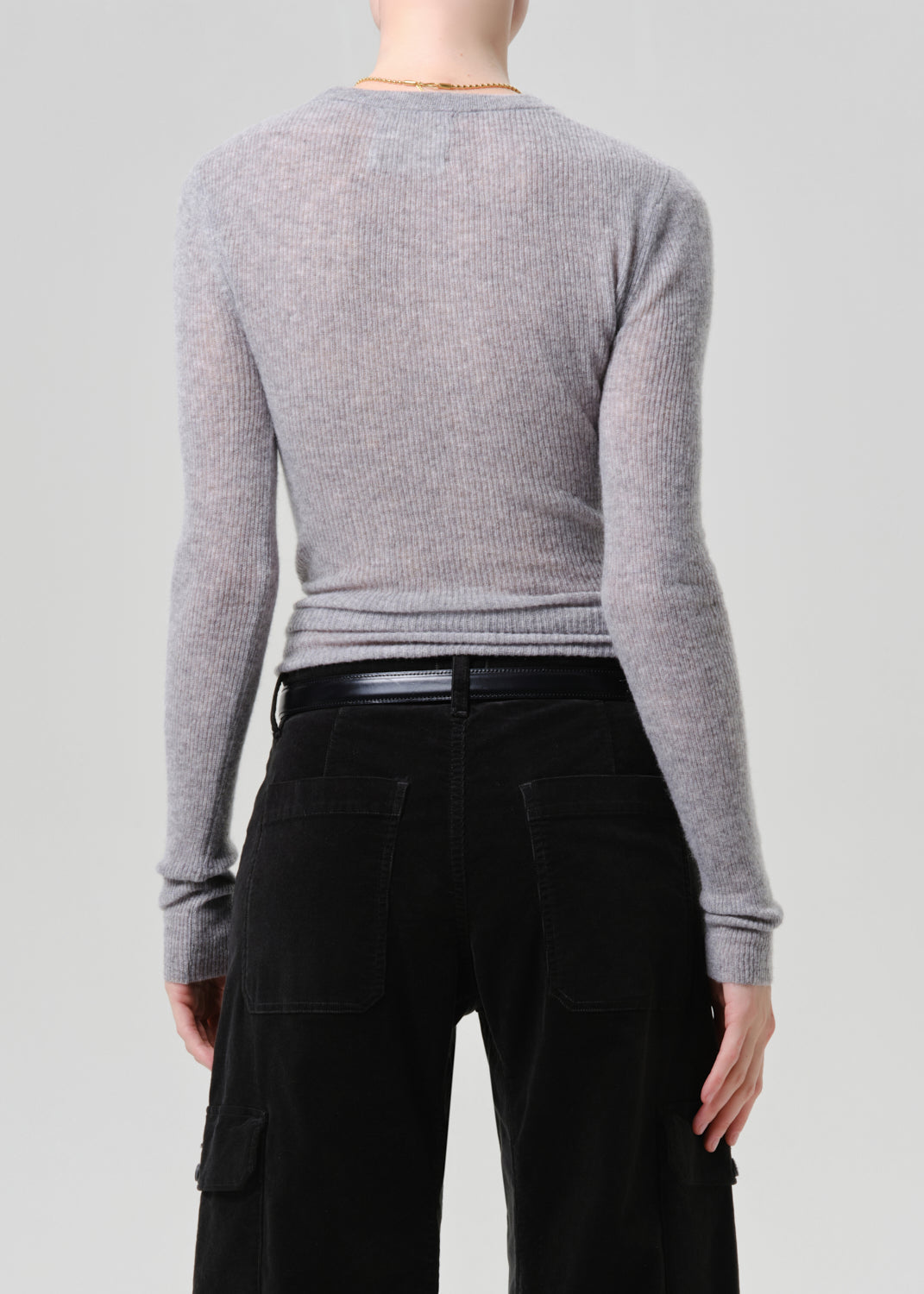 A model shown from the back wearing a light grey ribbed knit long-sleeve top and black pants against a grey background.