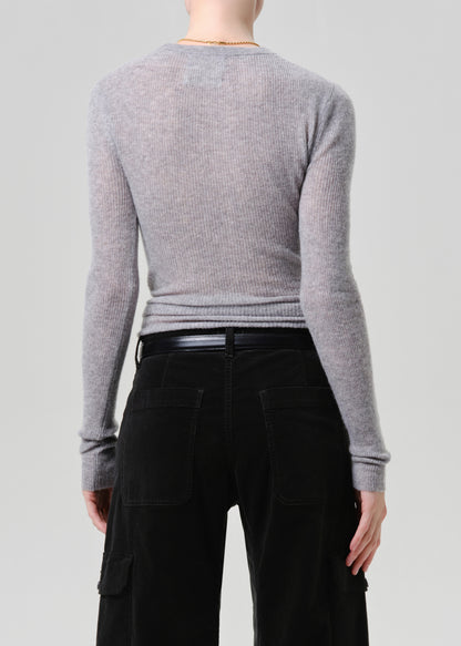 A model shown from the back wearing a light grey ribbed knit long-sleeve top and black pants against a grey background.