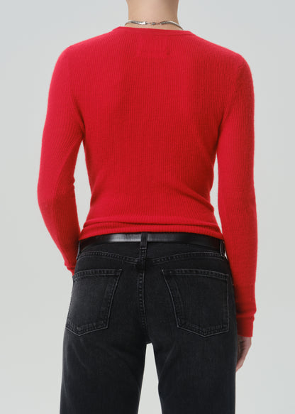 A person shown from the back wearing a bright red ribbed long-sleeve sweater and dark jeans against a grey background.
