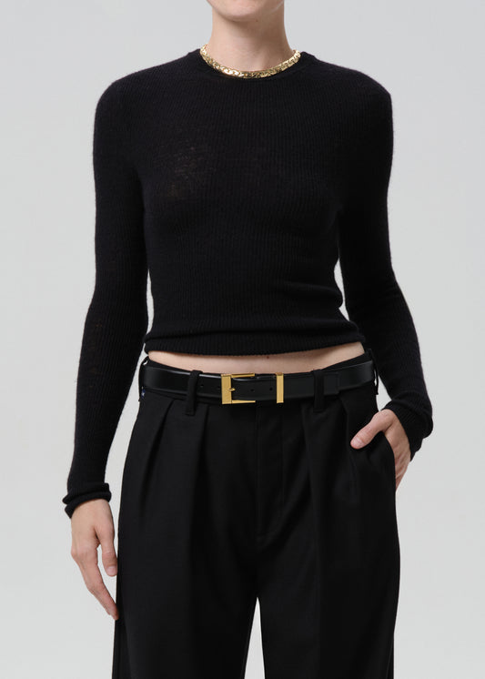 Person wearing black sweater with black belt and black pants on a grey background