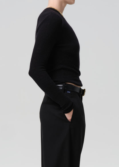 Side of person wearing black sweater with black belt and black pants on a grey background