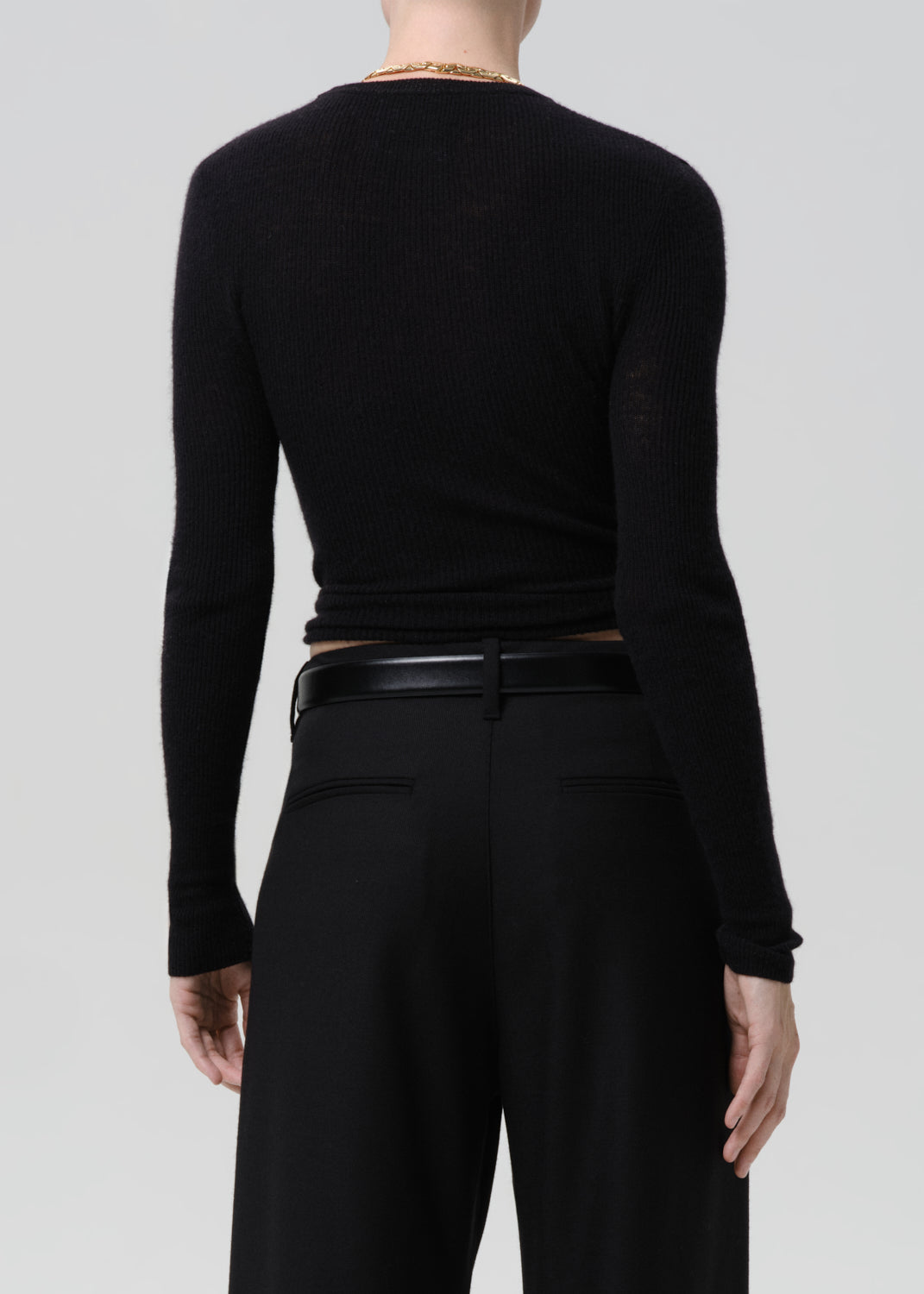 Back of person wearing black sweater with black belt and black pants on a grey background