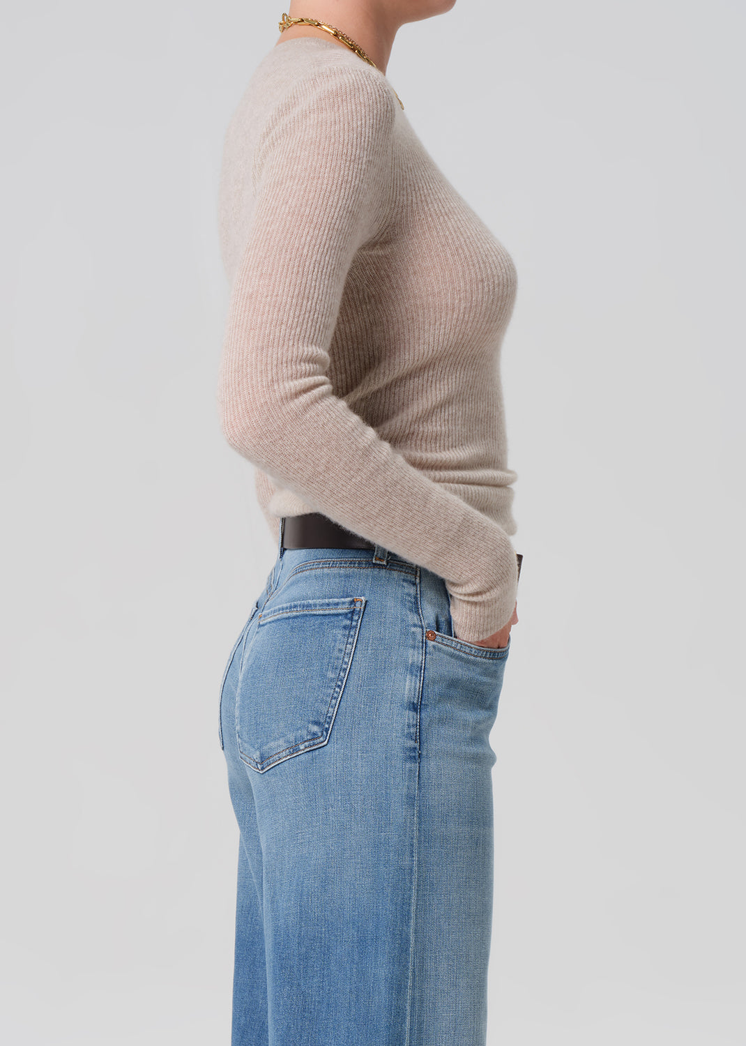Person wearing a beige sweater and blue jeans on a light gray background