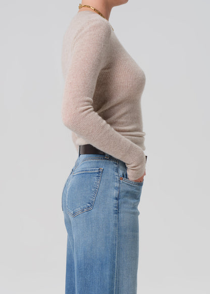 Person wearing a beige sweater and blue jeans on a light gray background