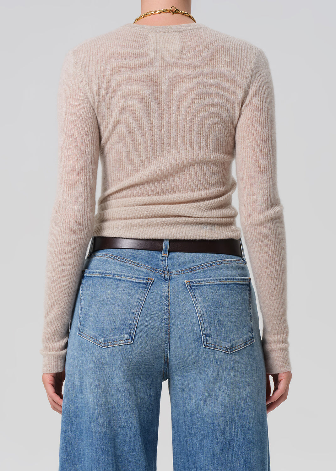Person wearing a beige sweater and blue jeans against a plain background