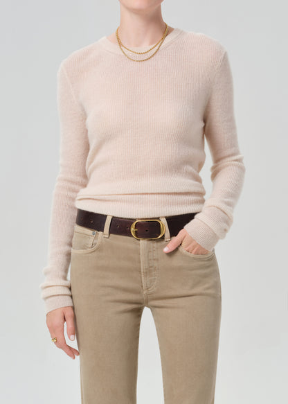 Person wearing a beige sweater and tan pants with a plain background
